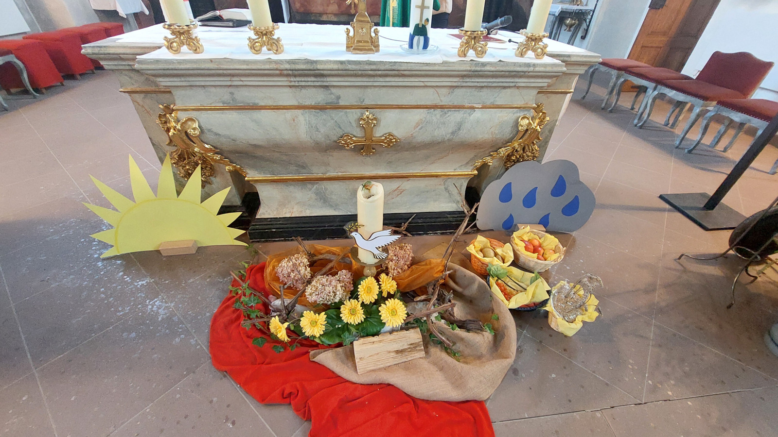 Kirchenaltar mit Erntedankdekoration mit Sonnen- und Regentropfensymbolen, Obst und Brot.