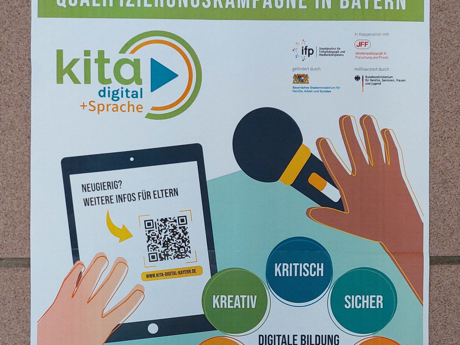 Ein Plakat mit Informationen zur Qualifizierungskampagne in Bayern, Featuring ein Tablet und bunte Sprechblasen mit Wörtern wie kreativ, kritisch und sicher.