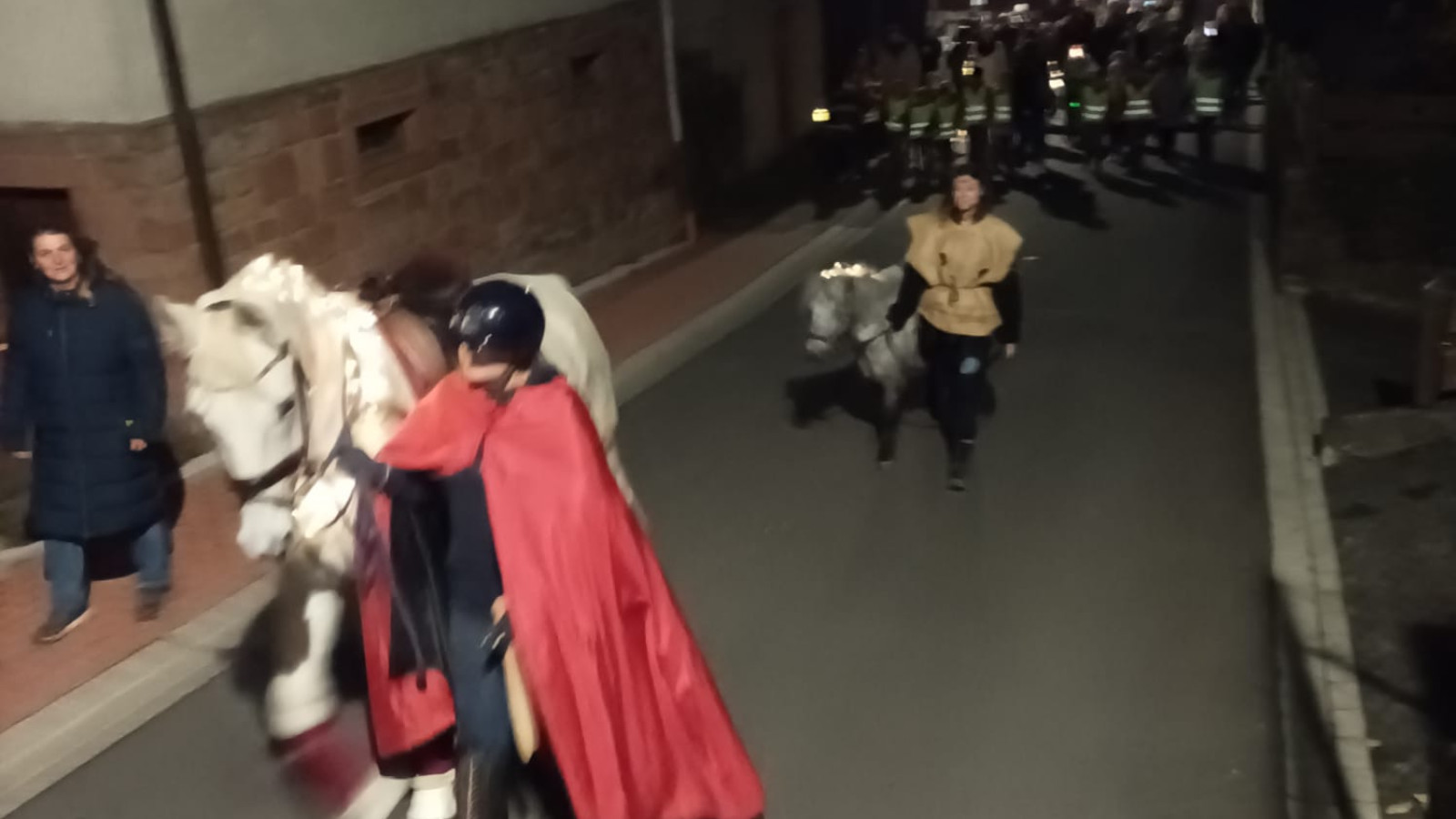 Reiter mit rotem Umhang führt eine Gruppe bei einem Laternenumzug in der Dämmerung an.