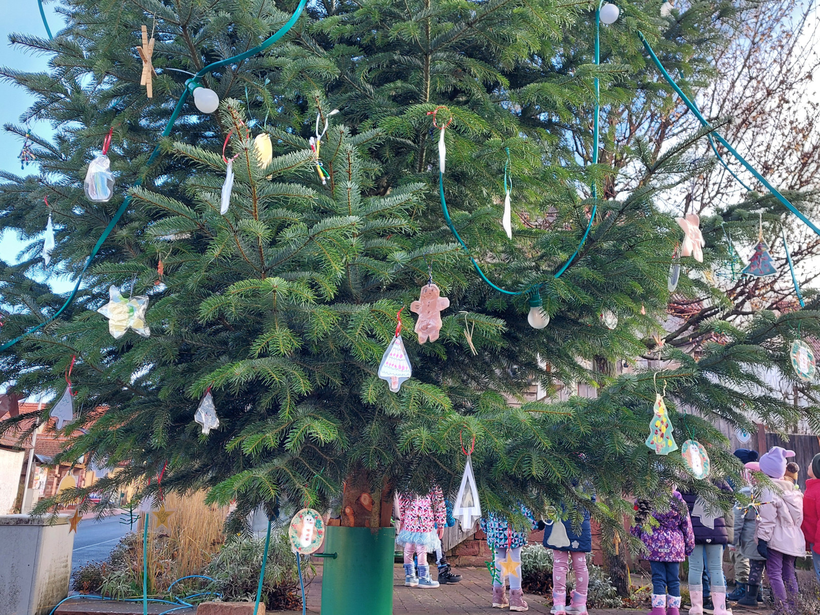 Kinder stehen um einen großen Weihnachtsbaum mit handgemachten Ornamenten.