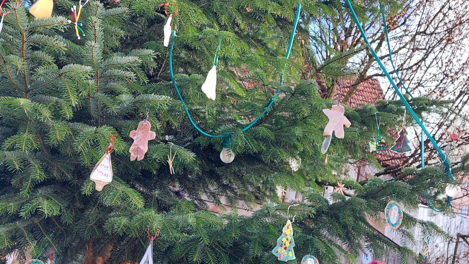 Kinder schmücken einen Weihnachtsbaum im Freien mit Ornamenten und Lichtern.