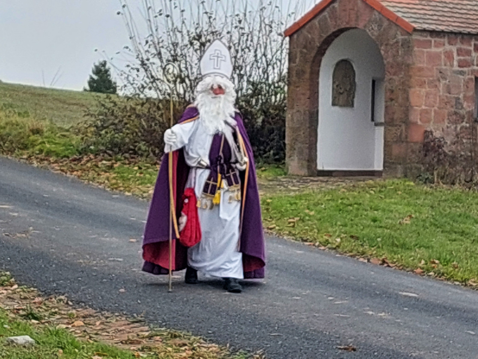 Person in Nikolauskostüm mit weißem Bart und Bischofshut auf einem ländlichen Weg.