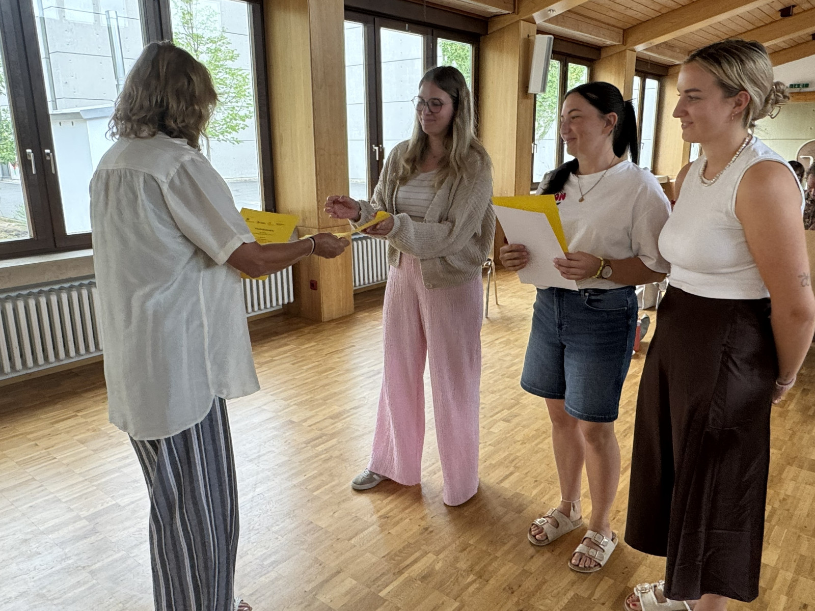 Vier Frauen in einem Raum. Eine Frau überreicht den anderen drei Dokumente.