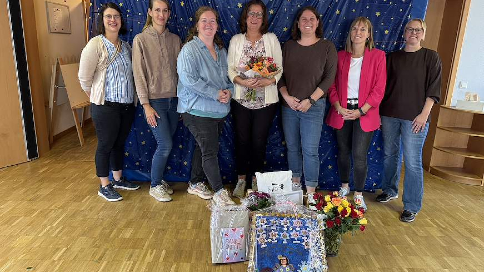 Sieben Frauen posieren vor einem blauen Vorhang mit Sternen, Blumen und Geschenke liegen vorne.